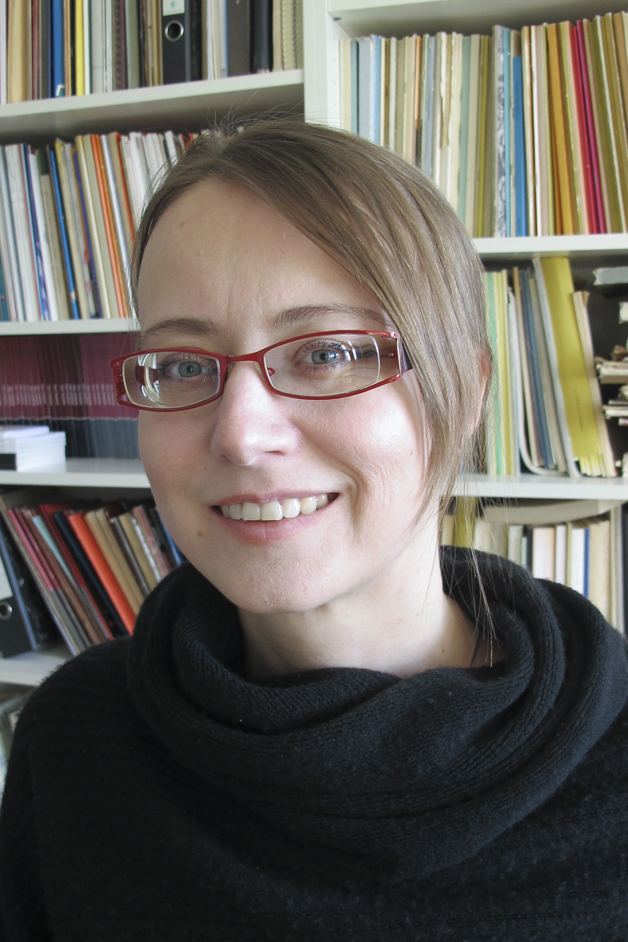 Woman with glasses stands in front of a shelf with books and sheet music.