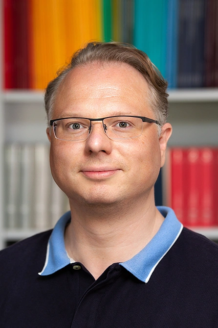 Porträt eines Mannes mit Brille vor buntem Bücherregal.